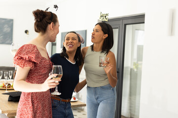 Laughing and holding drinks, three young women enjoy casual gathering at home