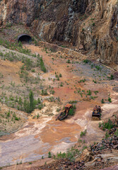 In the former copper mine of Falun Sweden, rusted vehicles lie amid a colorful red soil landscape of minerals. A bulldozer and crater showcase the site’s industrial past and nature's reclamation