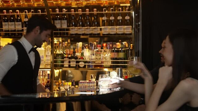 Smart bartender serving gin fizz or tonic with sliced lemon at luxurious bar, engaging lively conversation with VIP customer couple at side view in atmosphere at lighting warm nightclub. Vinosity.