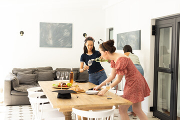 Setting table with wine glasses, three young women prepare for gathering at home