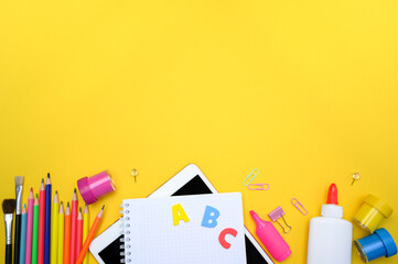 Back to school flat lay with ABC letters and educational tools on yellow desk. Contains pencils,...