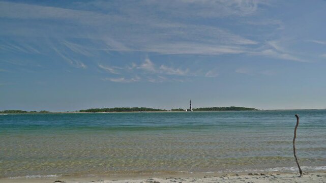 Wide shot of the diamond patterned lighthouse of Cape Lookout, North Carolina, stands in the back ground across the turquoise blue water of the Core Sound, as seen from Shackleford Banks.