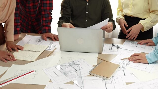 Smart architect and safety engineer discussion about building plan on table with architectural document, measurement tools and wooden block scatter around at modern office. Closeup. Delineation.