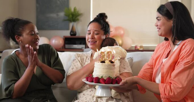 Three happy multiracial and black female friends with baby blowing candles on birthday cake at a bir
