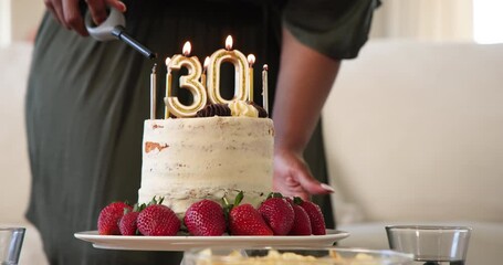 Happy black woman lighting candles with number 30 on birthday cake at a birthday party in sunny livi - Powered by Adobe