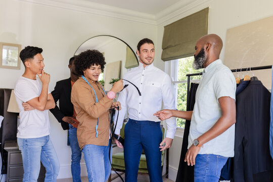 Groom trying on suit with friends offering advice and assistance at home - Powered by Adobe
