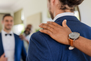 Groom receiving supportive pat on shoulder from friend before wedding ceremony