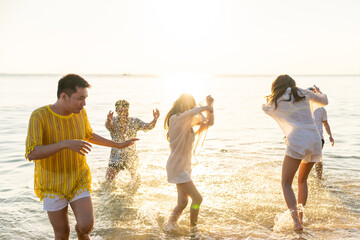 Happy Asian man and woman playing water in the sea on summer beach holiday vacation at sunset....