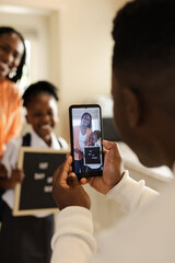 African American family capturing happy school moment with smartphone at home