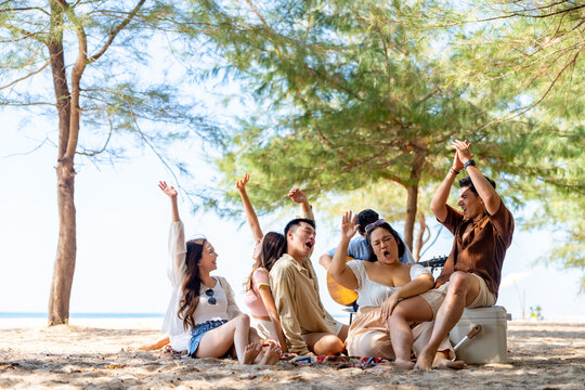 Happy Asian man and woman travel at the sea on summer beach holiday vacation. Group of People friends enjoy and fun outdoor lifestyle relaxing and picnic together on tropical island beach in sunny day