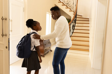 African American father talking to daughter with backpack in hallway before school