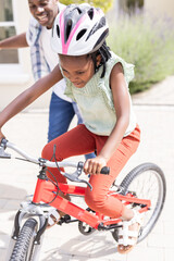 Fototapeta premium Father supporting African American child riding bicycle outdoors, both smiling