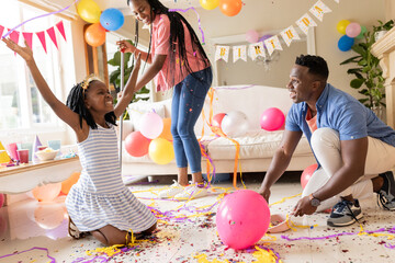 Celebrating birthday, family of three playing with balloons and confetti at home
