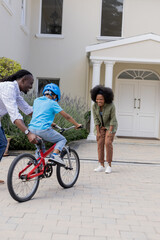 Fototapeta premium African American parents teaching child to ride bicycle in front of house