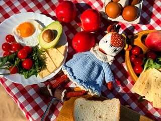 Cozy picnic setting with doll, fresh fruits, and breakfast items on checkered cloth