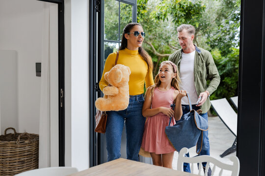 Family arriving home with bags and teddy bear, smiling and chatting together