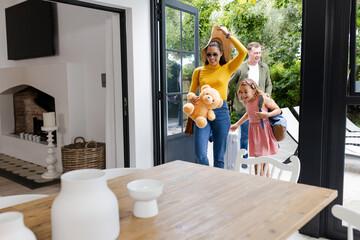 Family arriving home with luggage and teddy bear, smiling and excited