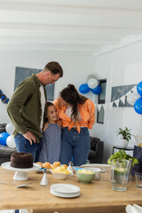 Family celebrating at home, smiling and embracing near decorated table with cake