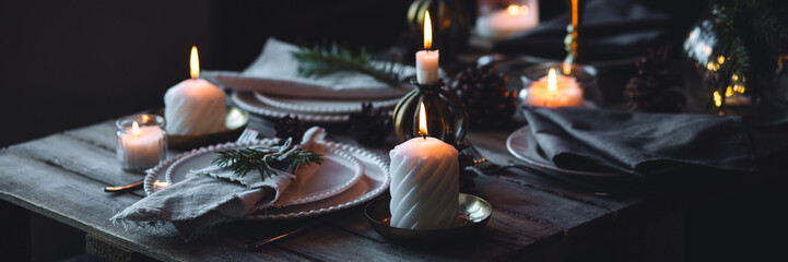 Banner. Beautiful table setting for family Christmas dinner at home. Cozy atmosphere, candlelight. Wine glasses, vintage chandelier, elegant interior. Fir tree branches, wooden furniture, dark, bokeh © ArtSys