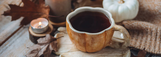 Spicy sweet fall hot drink: delicious strong herbal tea or coffee. Served in handmade artisan mug in shape of pumpkins, cozy home decor with candles, dry autumn leaves