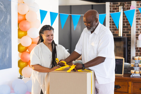 Elderly couple unwrapping large gift box at home, celebrating special occasion