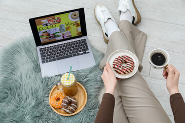 Blogger holding coffee and donut near laptop with food blog web site on floor indoors, above view