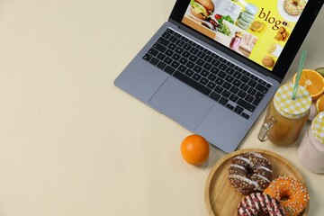Laptop with food blog web site, different drinks, fruits and donuts on beige background, above view. Space for text
