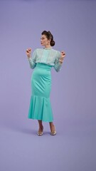 Young woman in vintage outfit and with glamorous hairstyle poses on purple studio background.