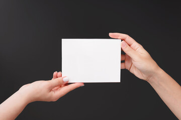 Female hand holds white cardboard packaging for skincare cosmetics or medicine on dark grey background. Packaging for pills or capsules