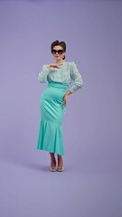 Young woman in vintage outfit and with glamorous hairstyle poses on purple studio background.