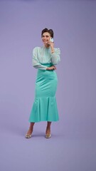 Young woman in vintage outfit and with glamorous hairstyle poses on purple studio background.