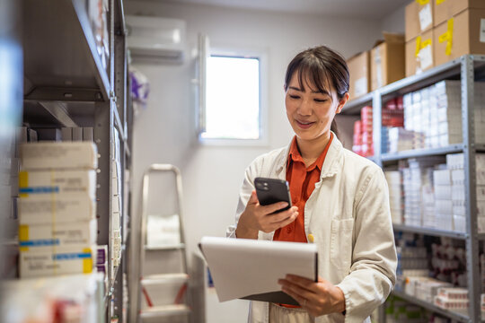 Smiling japanese woman in pharmacy hold mobile phone and clipboard