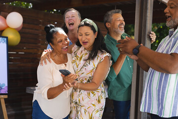 Seniors celebrating together outdoors, laughing and sharing moments with smartphone