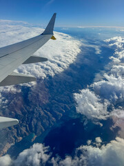Fototapeta premium AERIAL: View through window of a commercial plane flying above Croatian coast. Wispy clouds drift over rugged coastal landscape and Adriatic Sea, while a section of the airplane wing peeks into frame.