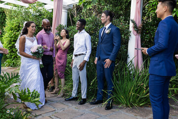Bride in white dress walking towards groom in blue suit, guests smiling warmly