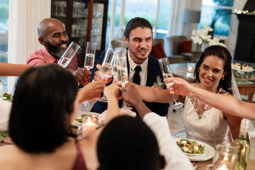 Toasting with champagne, diverse friends celebrating wedding around elegant dinner table