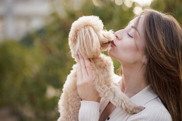 Woman kissing her cute dog, showing love and affection in a warm outdoor moment.