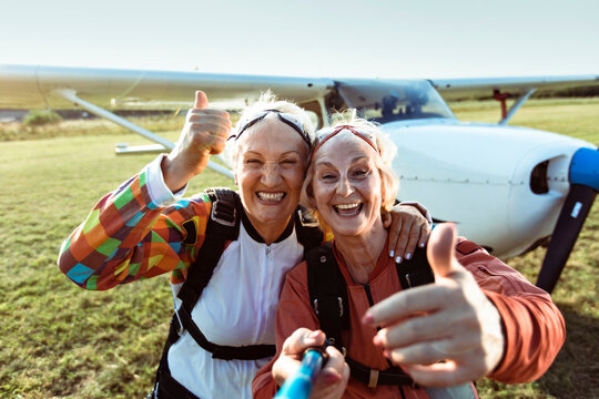 Senior lesbian couple taking a selfie with a smart phone after skydiving on a open field with an airplane in the background