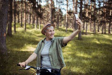Senior woman taking a selfie in forest while cycling on a summer day