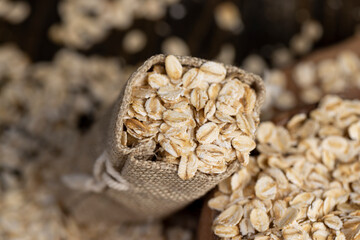 one linen bag with flakes for making porridge, scattered dry cereal flakes from oats, flattened, steamed and dried, closeup