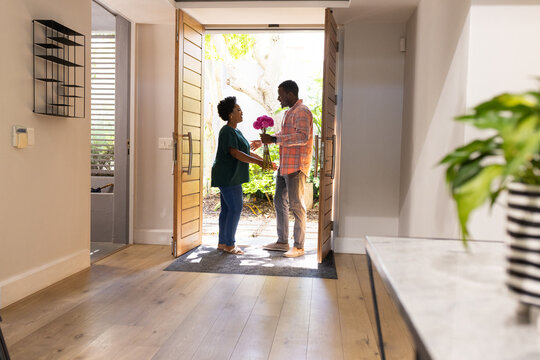 African American couple exchanging flowers at home entrance, sharing joyful moment - Powered by Adobe