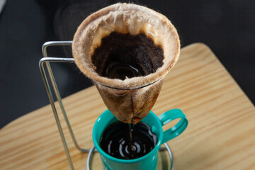 Xícara de café verde esmaltada recebendo café fresco de um coador sobre uma superfície de madeira.