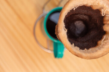 Visão próxima de um coador de café em uso, preenchendo uma xícara esmaltada verde.