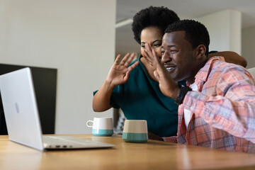 African American friends video chatting on laptop at home, smiling and waving