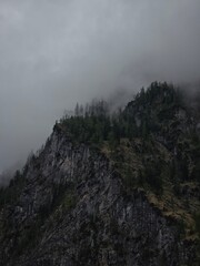 Mysterious black cliffs rise above Obersee, shrouded in thick mist, creating a dramatic and moody alpine scene in Berchtesgaden National Park, Bavaria, Germany.