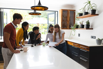Teens in kitchen celebrating good news, smiling and reading letter together