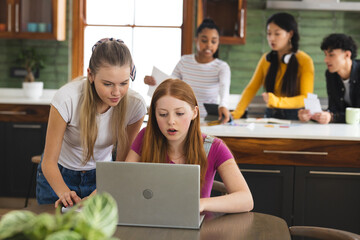 Teen girls using laptop in kitchen while friends collaborate on school project