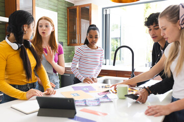 Teen friends in kitchen discussing project, using tablet and papers, looking engaged © wavebreak3