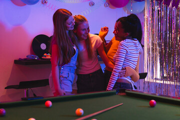Fototapeta premium Teen girls laughing and hugging near pool table at vibrant party celebration