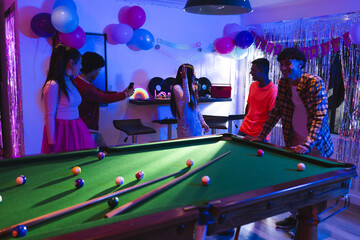Fototapeta premium Teenagers celebrating at home, playing pool and taking photos with friends